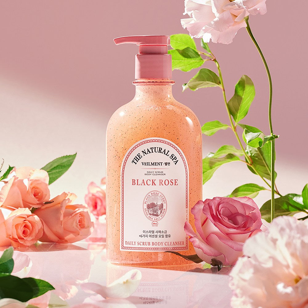 Veilment Black Rose scrub body wash standing among pink roses and green leaves on a reflective surface
