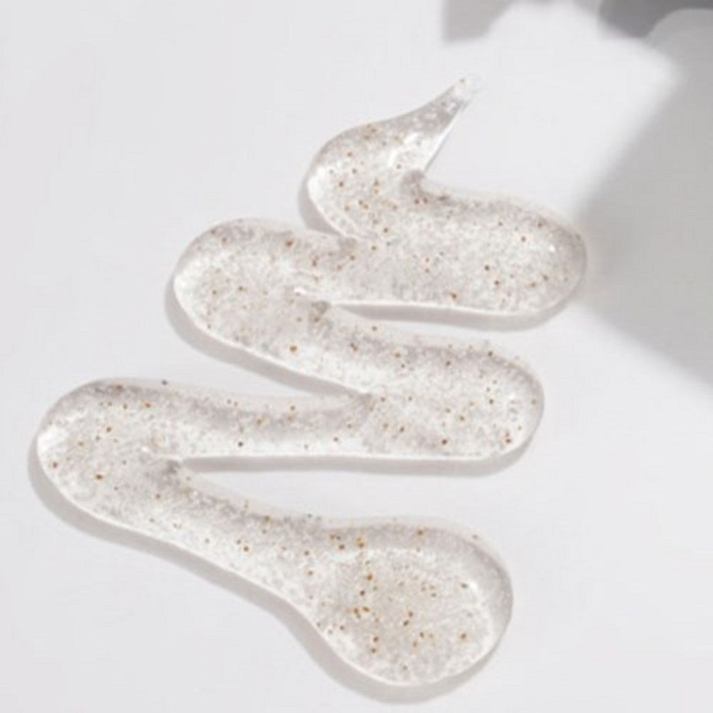 PLU scrub body wash texture in a winding clear gel smear with small brown grains on a white surface