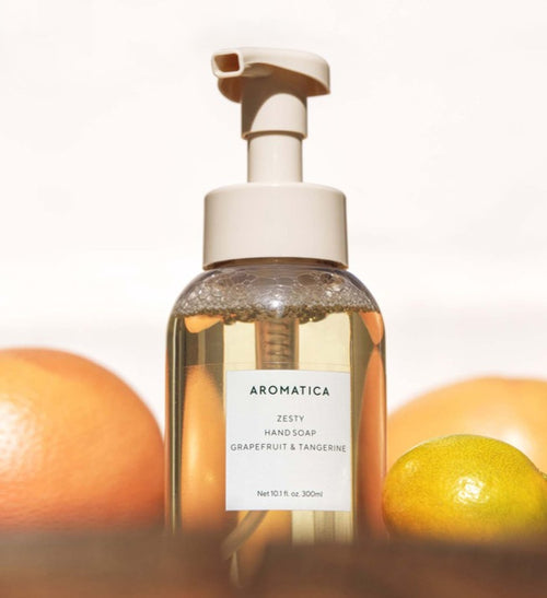 AROMATICA Zesty Hand Soap in a clear pump bottle surrounded by citrus fruits, with bubbles above the liquid.