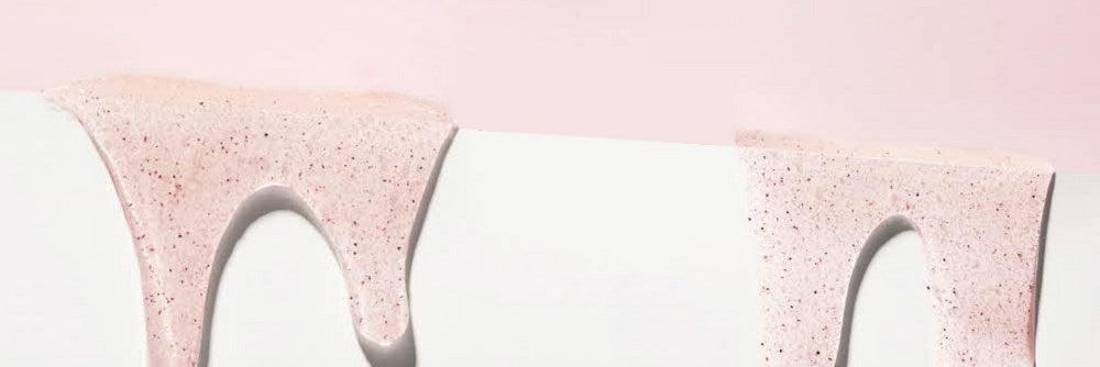 Veilment scrub body wash texture shown as pale pink gel with fine grains flowing over a white ledge
