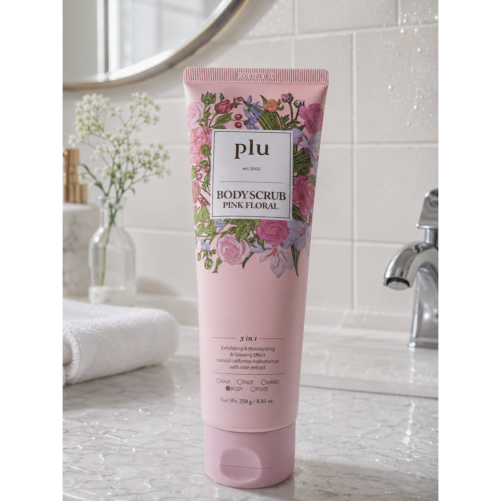 PLU Pink Floral Body Scrub pink tube standing on a wet bathroom counter beside a towel and tap