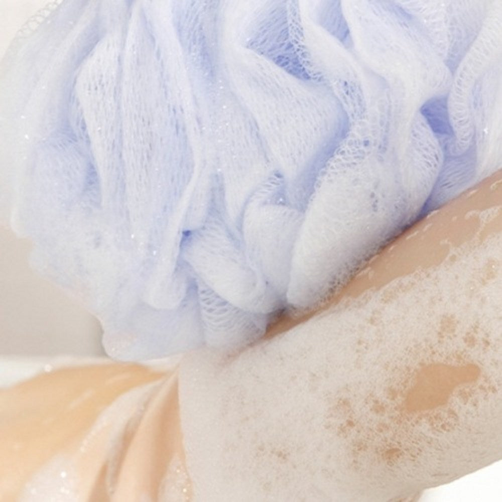 Veilment White Musk body wash lather on skin beneath a pale lavender mesh shower puff