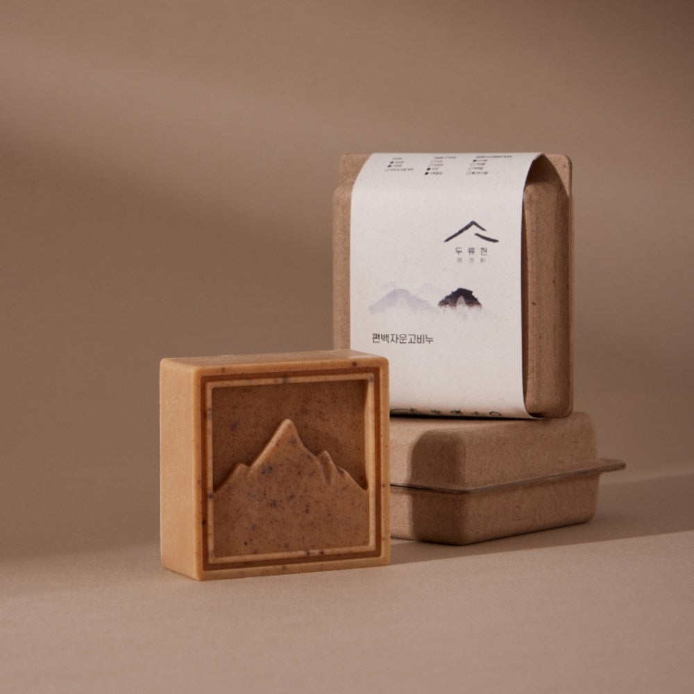 Dooryuheon Hinoki Cypress Soap with a brown, flecked mountain relief beside kraft packaging on a beige surface