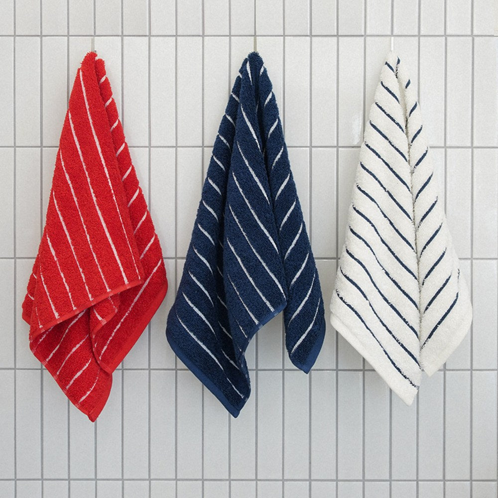 Towel Talk Seacline face towels hanging against white tiles in red, navy and white striped colourways