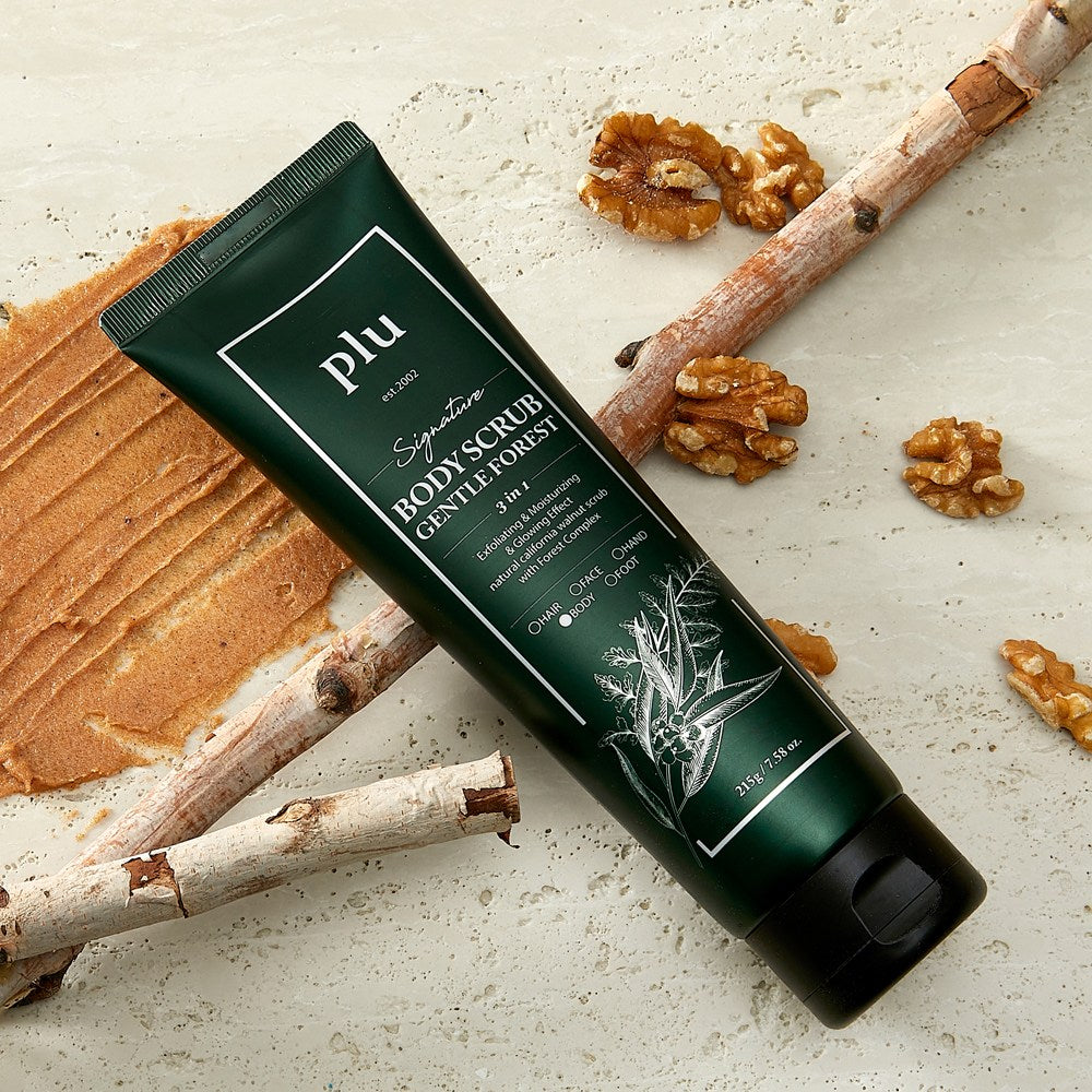 PLU Gentle Forest body scrub lying diagonally among branches and walnuts beside a brown scrub smear