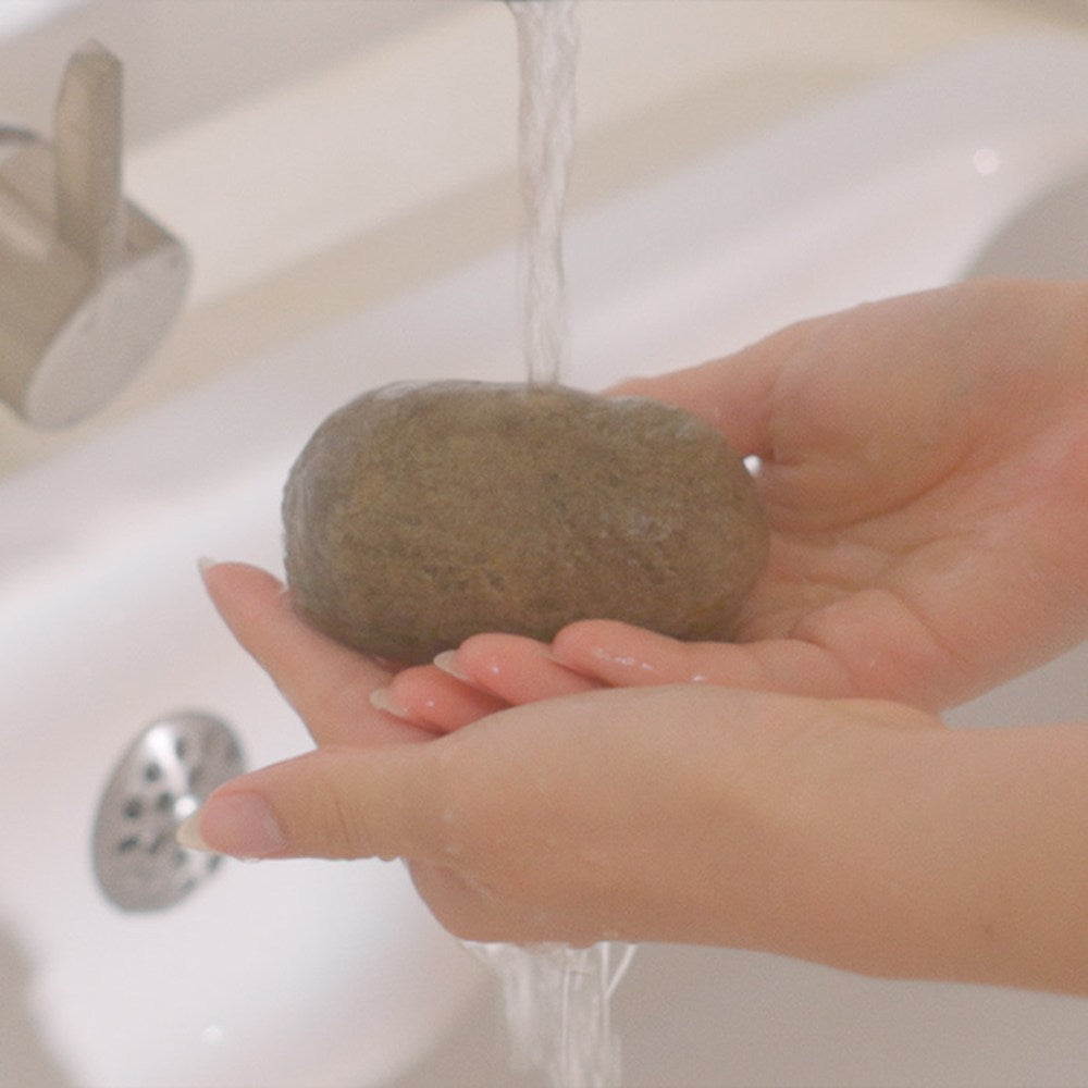 Jeongango extract soap cupped in two hands beneath running water in a white bathroom basin