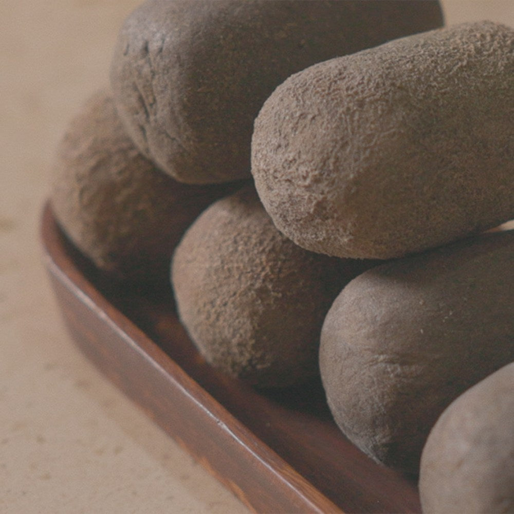 Jeongango extract soap bars stacked on a wooden tray, showing their rough brown surfaces and rounded edges