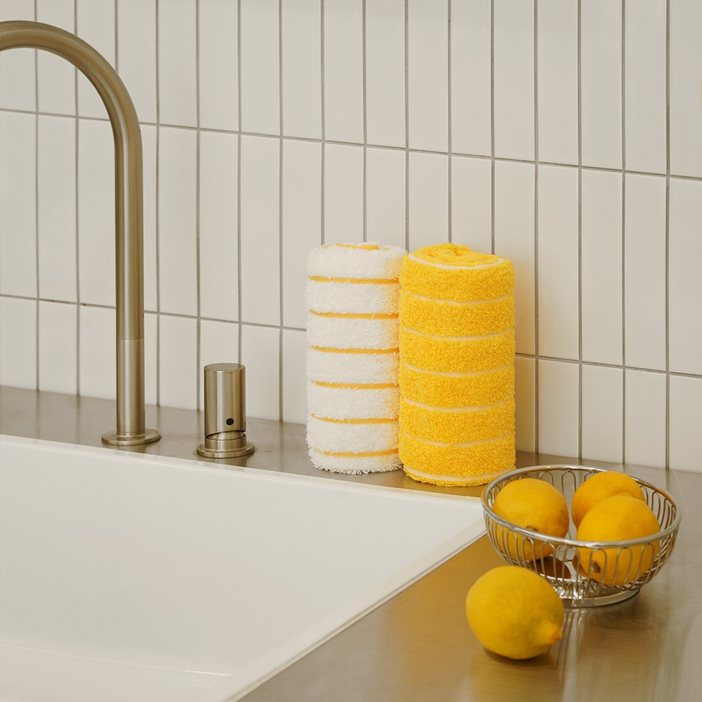 Towel Talk Seacline face towels rolled beside a sink in yellow and white, with lemons and a brass tap
