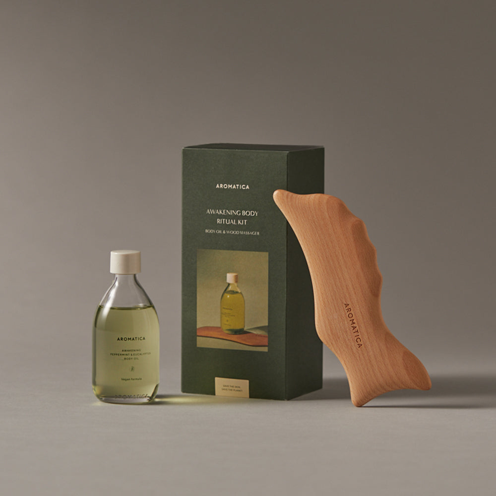Aromatica body oil ritual set with green-tinted oil, a dark green box and wooden dolphin gua sha on a grey surface