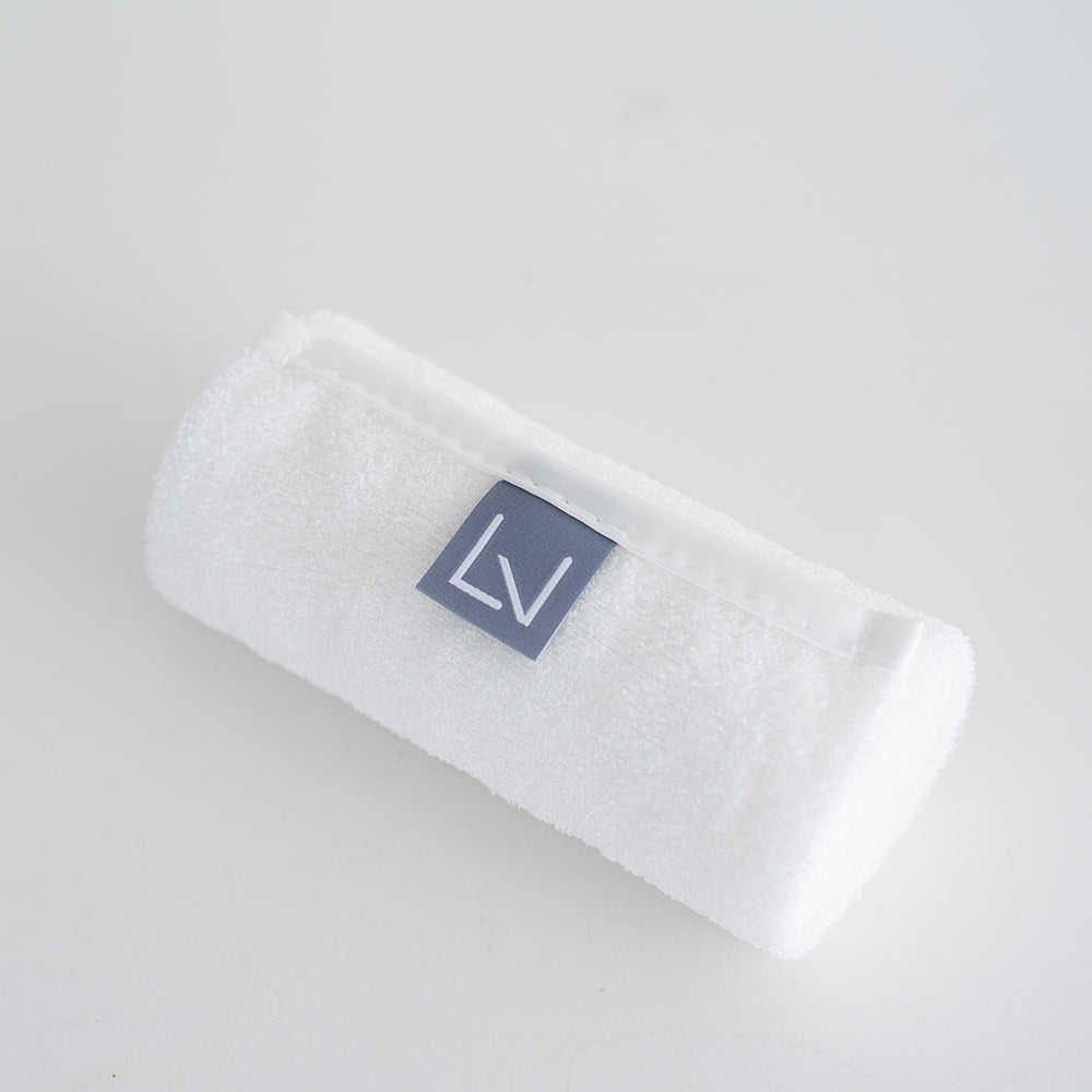 Purelevy exfoliating shower towel rolled on a pale surface, showing white fabric and a grey logo tab