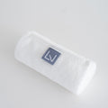 Purelevy exfoliating shower towel rolled on a pale surface, showing white fabric and a grey logo tab