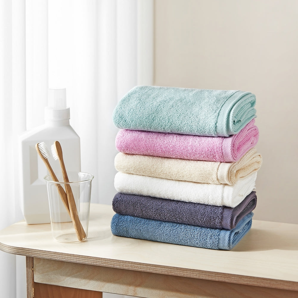 Songwol towel set stacked in mint, pink, cream, white, charcoal and blue beside toothbrushes and a white bottle