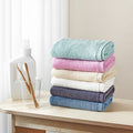 Songwol towel set stacked in mint, pink, cream, white, charcoal and blue beside toothbrushes and a white bottle