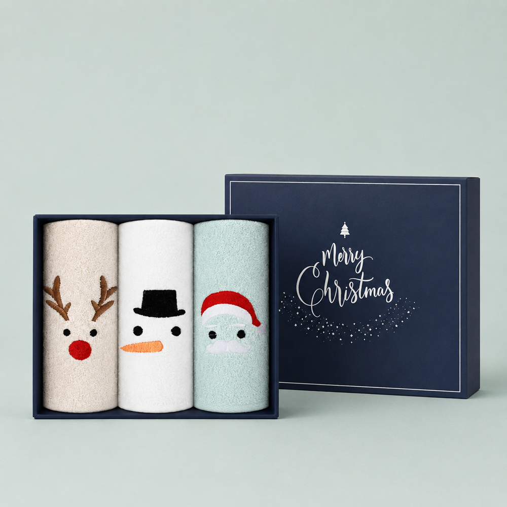 Songwol Christmas towel set with cream Rudolph, white Snowman and mint Santa towels beside a navy gift box