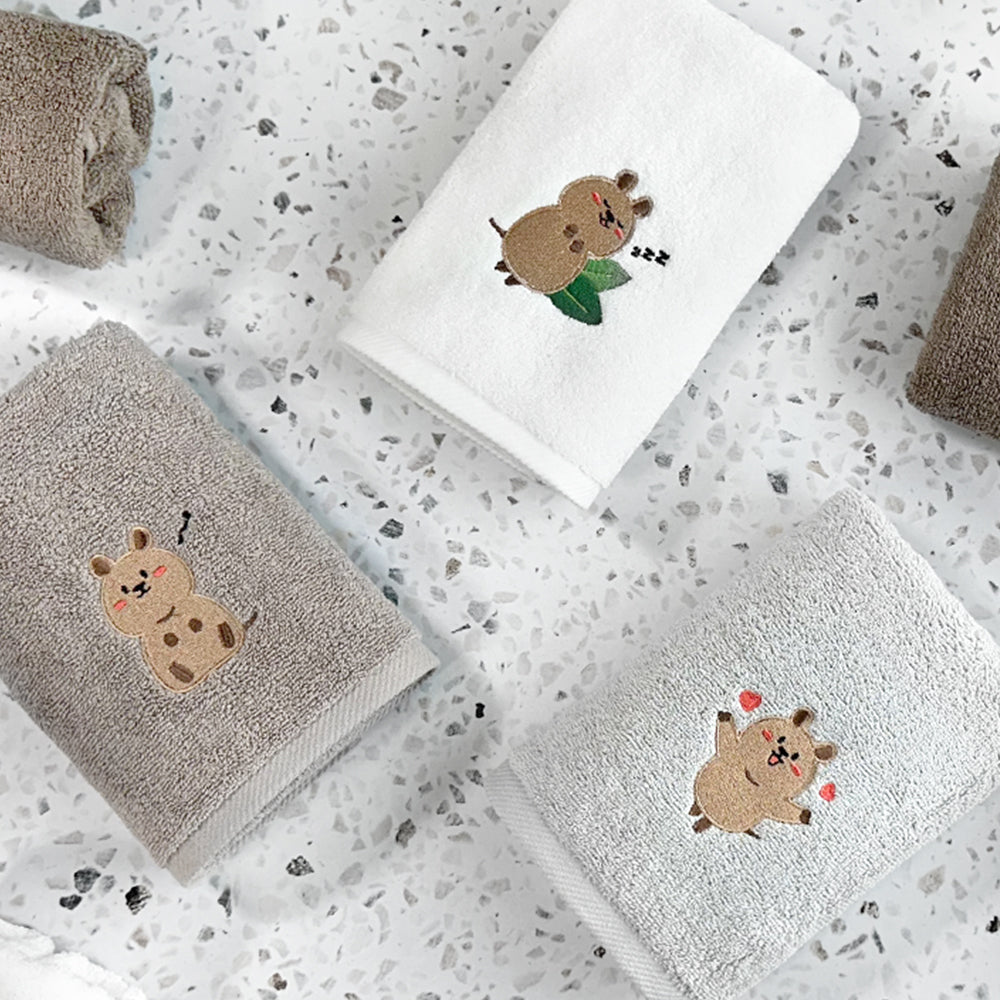 Songwol Quokka face towels folded on a speckled surface, showing sleeping, seated and heart-themed characters