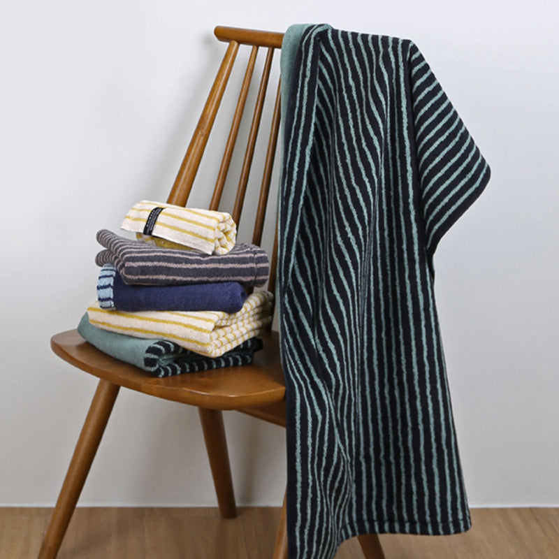 Songwol Solid Stripe 68 bath towel in dark and mint stripes draped over a wooden chair beside folded towels
