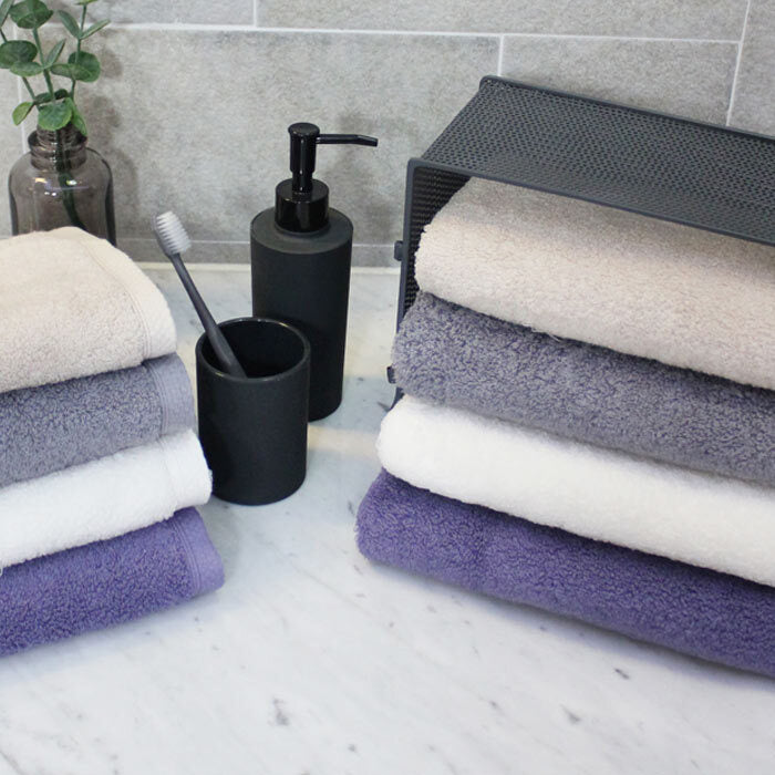 Songwol combed cotton bath towels arranged in two stacks beside black washbasin accessories and a plant
