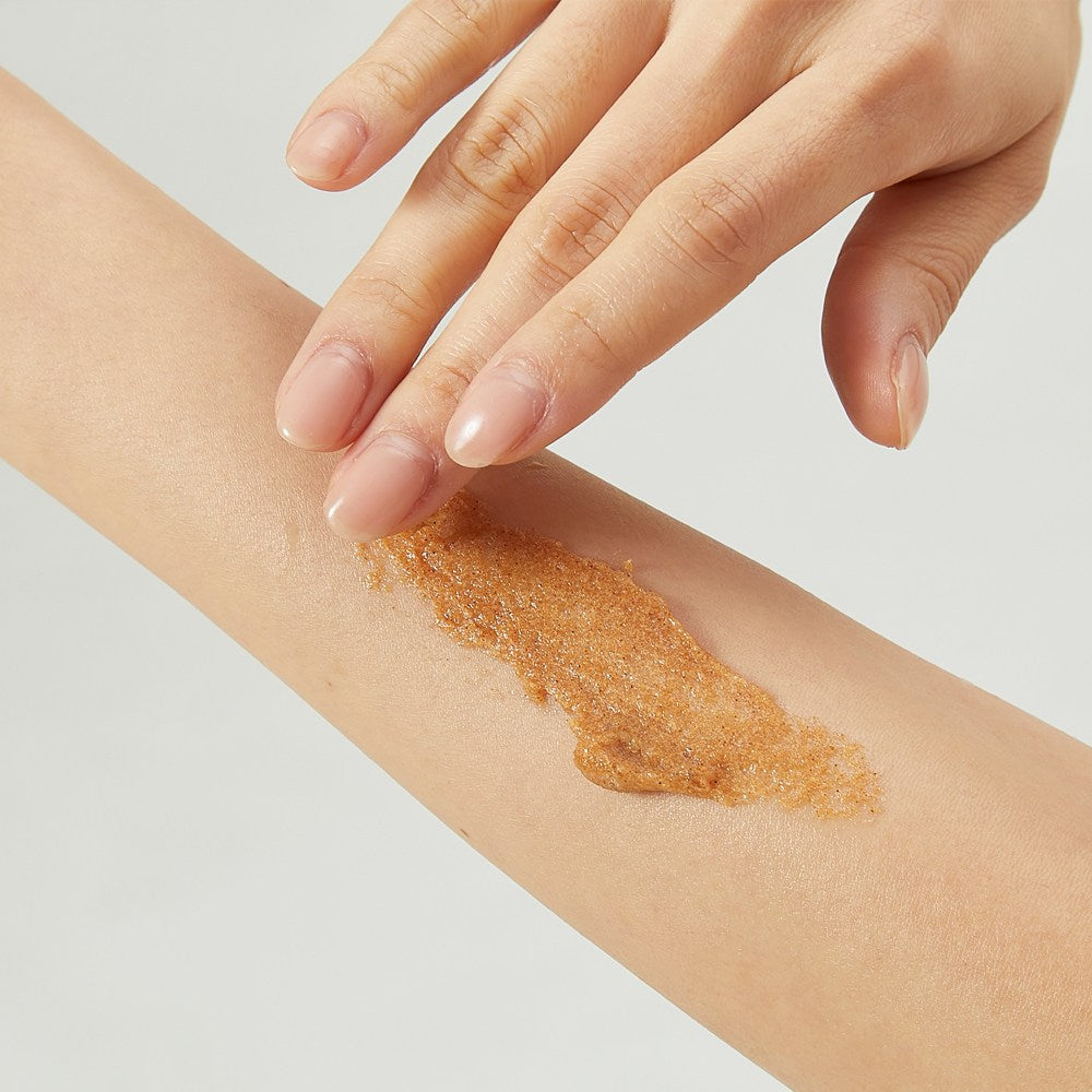 PLU Gentle Forest body scrub being massaged onto a forearm, showing its brown, grainy texture