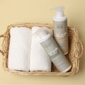 Boryeong Mud Treatment beside a matching shampoo bottle and folded white towels in a wicker basket on a yellow background
