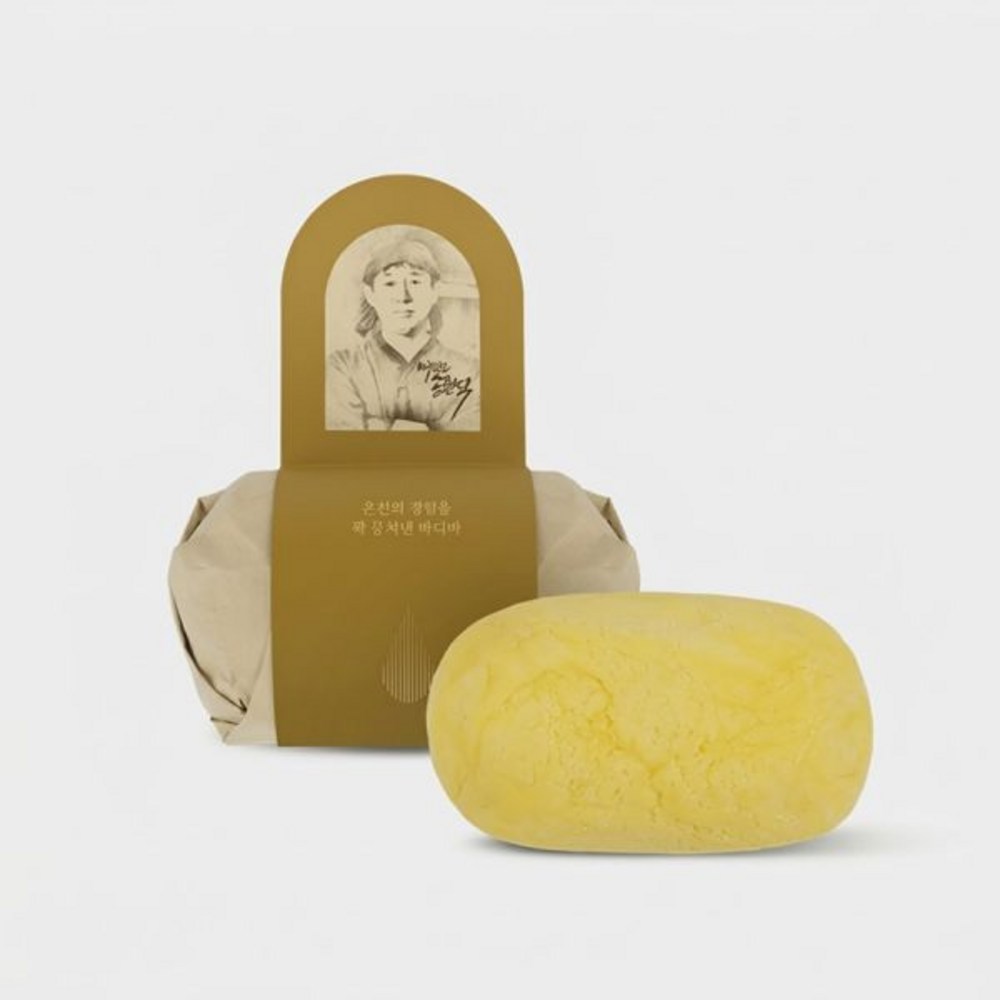 Cheonbinusop Oncheongo body soap bar in yellow beside cream paper wrapping with a gold band and portrait
