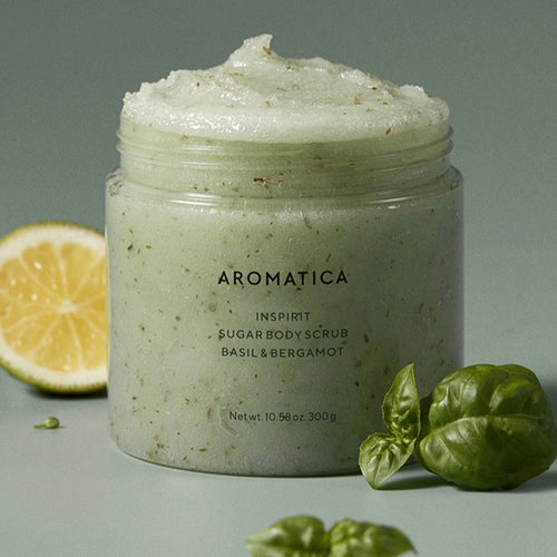 AROMATICA Inspirit Sugar Body Scrub in an open jar, showing its flecked green texture beside citrus and basil.