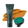 PLU scalp scrub in a dark green tube beside a green-tipped massage brush and an orange-brown textured smear