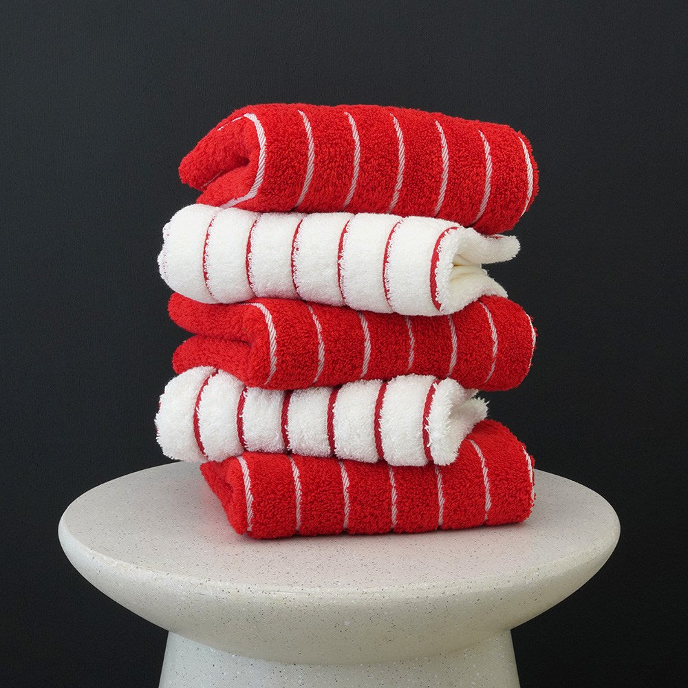 Towel Talk Seacline face towels stacked in red and white stripes on a pale pedestal against a dark background