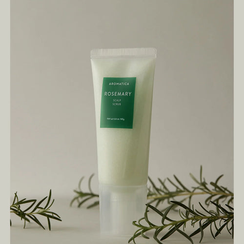 Aromatica rosemary scalp scrub tube standing among rosemary sprigs against a muted beige background